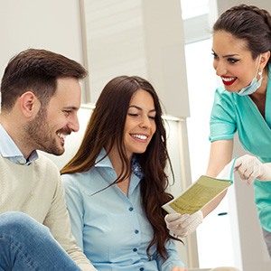 Smiling couple reviewing paperwork with dental assistant